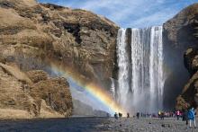 A group of people standing at base of the waterfall with rainbow over them